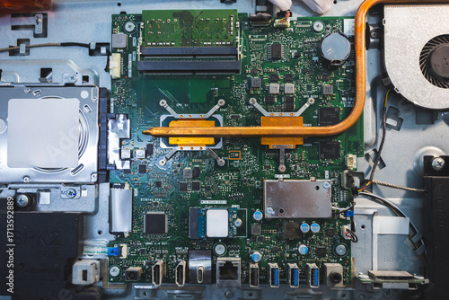 Close-up image of an all-in-one computer interior showing the motherboard, heat pipe cooling system, RAM slot, processor, and electronic components. Inside View of All-in-One Computer Motherboard
