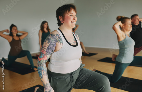Body positive young woman with tattoos smiling while taking a yoga class with other female students in a studio