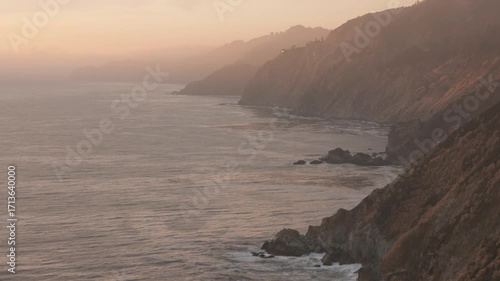 HD ground-level footage of a spectacular sunset over the Pacific Ocean, filmed from the rugged Big Sur coastline in California. The clip captures the dramatic colors of the sky, the sun dipping into t