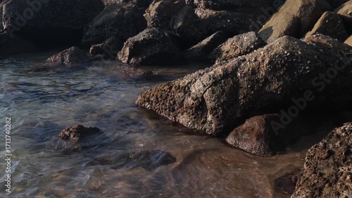 Waves crash against rocks at beach, sea spray air. Natural ocean wave motion, hit rough stone coast. Travel atmosphere