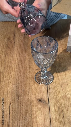 A set of glass goblets. A woman unboxing and reviewing stemmed glass goblets. Vertical video. Close-up