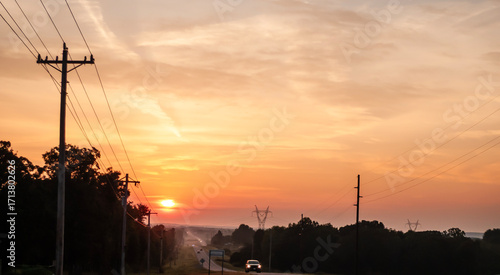 Morning Drive in the country at sunrise. September morning drive, beautiful sunrise, view from a hilltop in the country, power lines framing the roadway with a vehicle coming toward the viewer.
