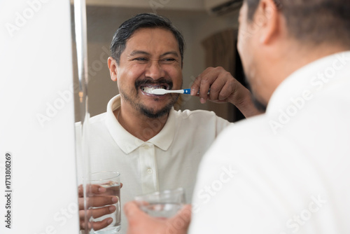 Photography Smiling man brushing teeth in front of bathroom mirror holding glass of water fo
