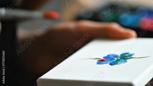 Wallpaper Mural Artist's hand carefully painting a vibrant blue and red flower on a small white canvas Torontodigital.ca