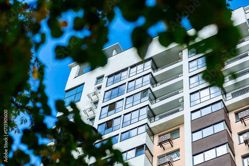 A modern residential building with large windows, balconies of varying depths, a light-colored façade, and surrounding greenery. The architecture emphasizes comfort and style.