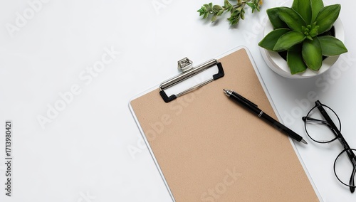 Flat lay of a clipboard, pen, glasses, and plant on white background