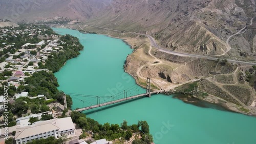 A scenic aerial view of the Naryn River flowing between a village and a winding mountain road, connected by a bridge.