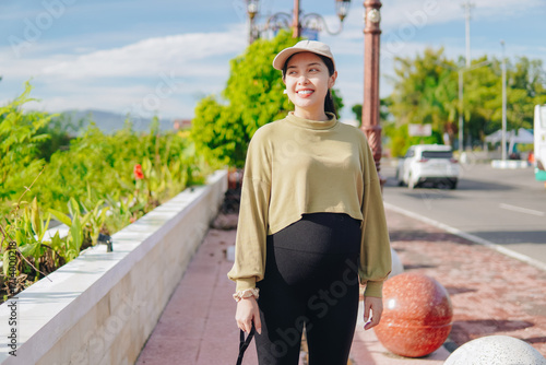 Beautiful young Asian pregnant woman doing morning jogging exercise, posing with nature background.