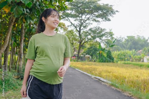 Beautiful young Asian pregnant woman doing morning jogging exercise, posing with nature background.