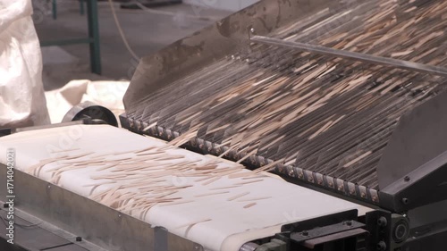 Conveyor belt moving wooden ice cream sticks in workshop of woodwork factory. Automatic machinery equipment with production line. Industrial manufacturing of wooden products, timber, lumber in plant.