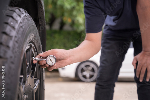 Photo of a young man checking the air pressure in his car tires by himself.