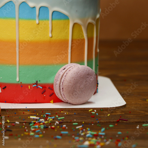 Konstfotografi Rainbow layer cake decorated with colorful dripping icing and scattered sprinkles on wooden surface