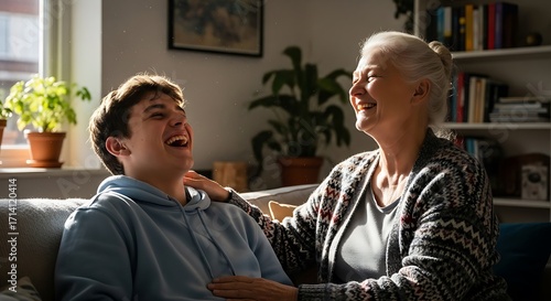 A happy grandmother and her teenage grandson share a joyful moment, laughing together on a sunlit couch at home.