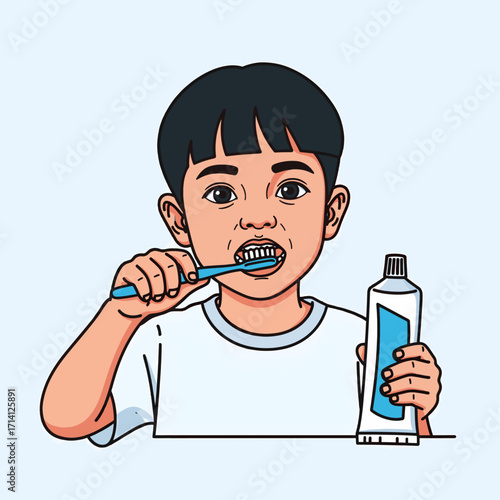 A young boy with dark hair is brushing his teeth with a blue toothbrush and holding a tube of toothpaste.