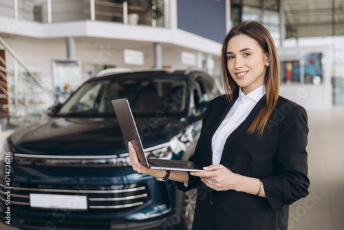 Saleswoman holding laptop in car dealership