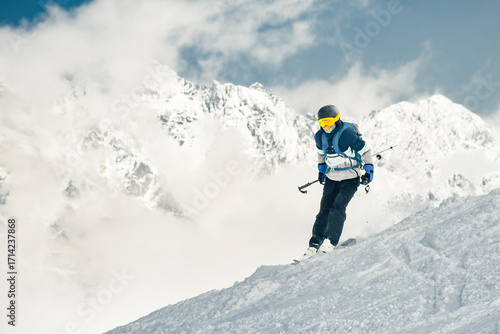 Male Skier in blue jacket speeding downhill on snowy mountain slope with scenic alpine peaks in background.Cinematic blue