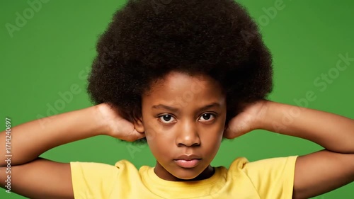 Close-up portrait of a young girl with afro covering her ears on a green background