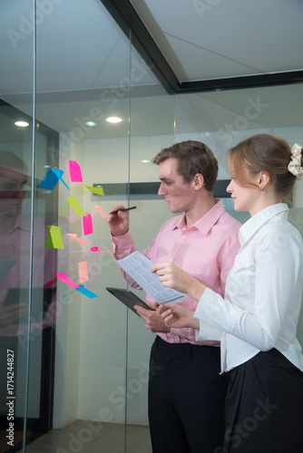 Creative professionals collaborate in modern office, using colorful sticky notes for brainstorming and planning. Their focused expressions reflect teamwork and innovation.