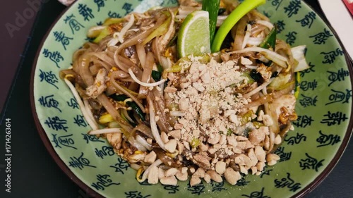 Close-up of Pad Thai with chicken, lime, peanuts, and vegetables in a decorative bowl, served with a glass of red lemonade. Traditional Asian meal with vibrant colors and textures