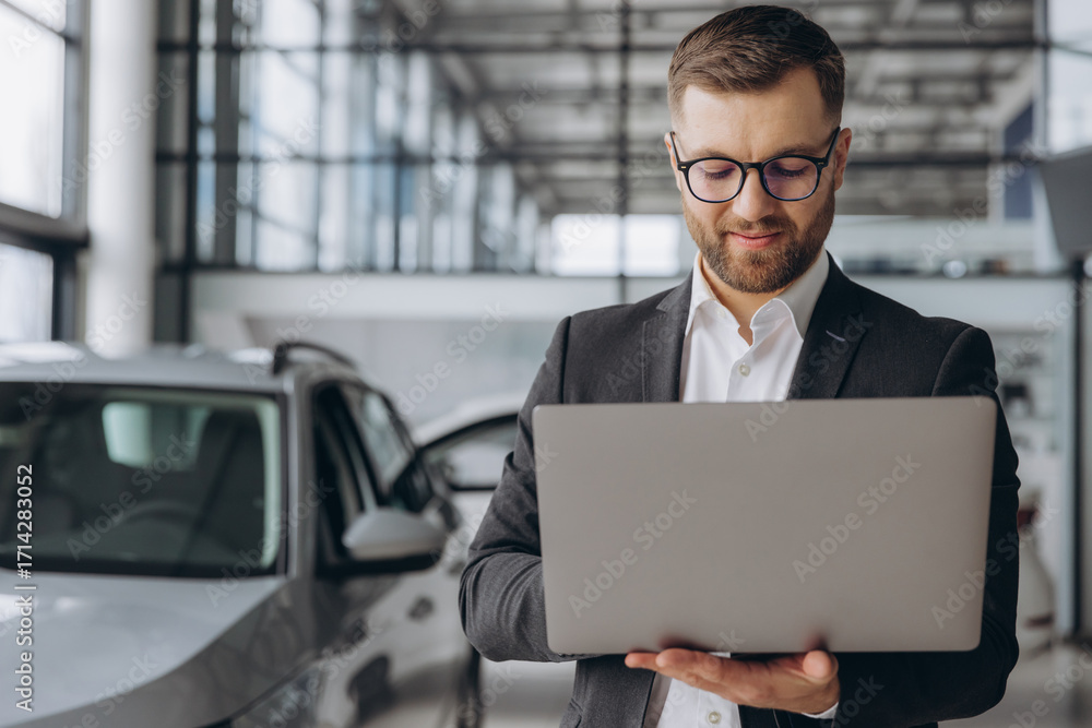 © anatoliycherkas - Modern bearded man in glasses and suit vehicle sales consultant using laptop inside car dealership © anatoliycherkas - Modern bearded man in glasses and suit vehicle sales consultant using laptop inside car dealership