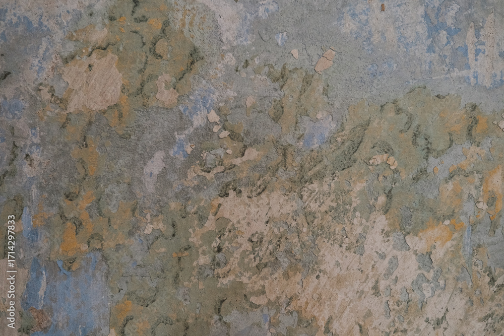 Fototapeta premium A close-up of a cracked, weathered wall surface with layered, peeling paint in earthy tones. Featuring a blend of blue and green textures, it's perfect for backgrounds or artistic applications.