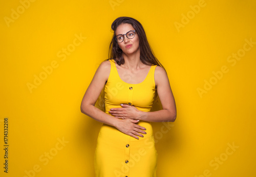 Stomach ache, woman suffering from stomachache, isolated on yellow background. Ill girl with chronic gastritis. Abdomen bloating concept.