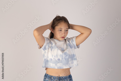 Young girl is posing with her hands behind her head,looking slightly downwards..