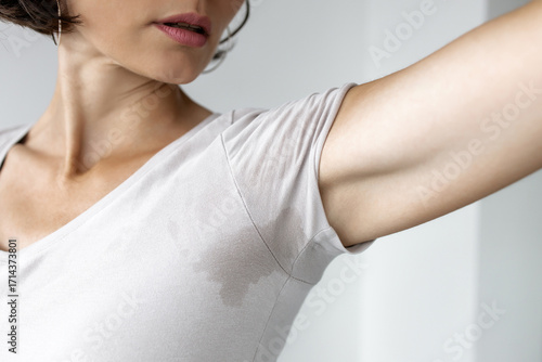 Woman checking sweat stain under armpit on her t-shirt, concept of excessive sweating, body odor and hyperhidrosis problem in adult female 