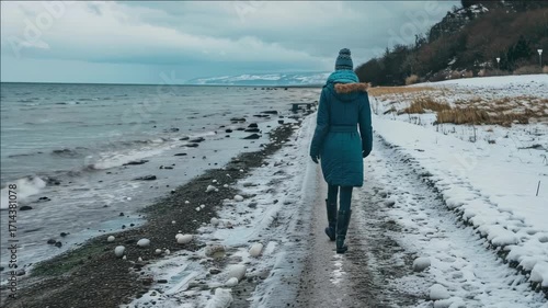 A person walking on the beach path amidst a wintery scene, with snow covering the ground and an overcast sky.