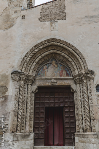 Wallpaper Mural View of a weathered stone archway frames a dark wooden door, topped by a faded fresco, a silent sentinel of history and art, Anversa degli Abruzzi, Abruzzo, Italy. Torontodigital.ca