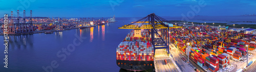Aerial view of international cargo containers ship at industrial import-export port prepare to load containers with big container loader ship vessel at night. global transportation, logistic business.