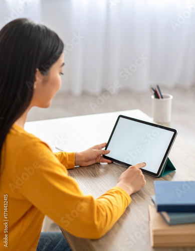 Teenager using tablet for online classes, sitting at home desk with books