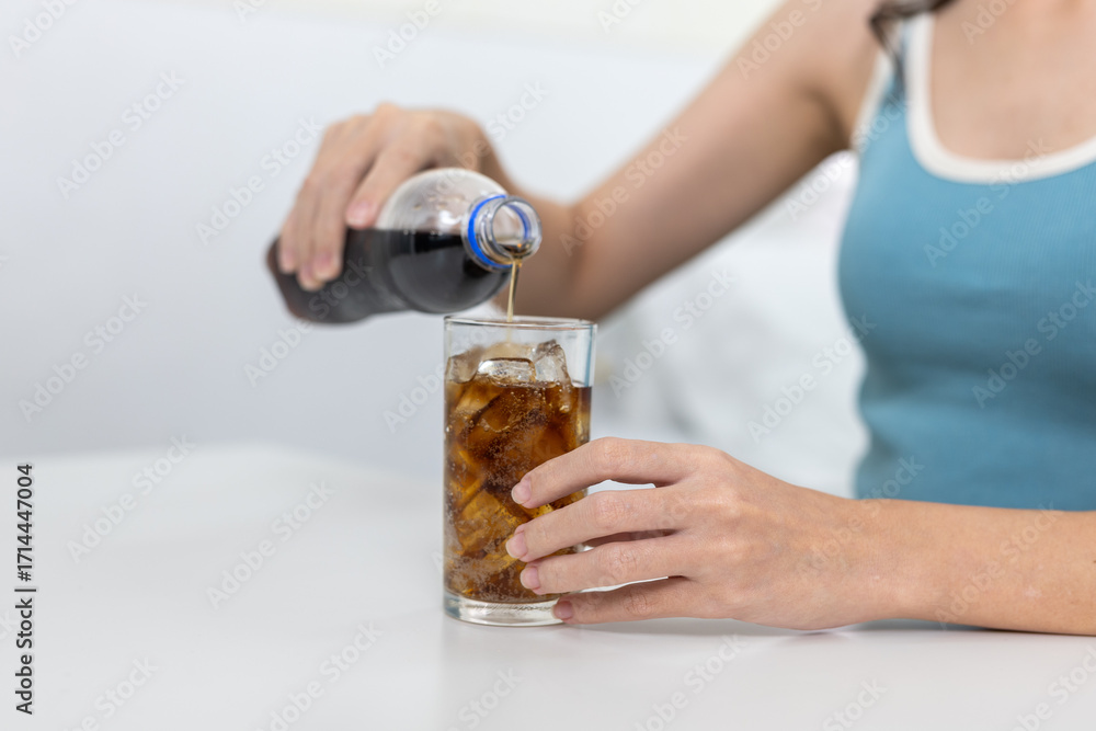 Fototapeta premium Close-up of women pouring dark soda into glass with ice. Refreshing but sugary beverage concept, lifestyle habit of soft drink consumption, and unhealthy drink choices in daily routine.