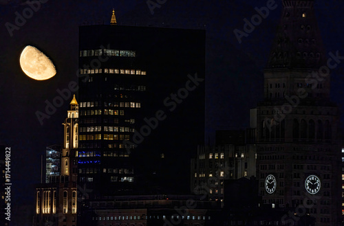 View of a waxing gibbous moon casting a soft glow over the dark silhouettes of buildings, creating a striking contrast in the night sky, New York, New York, United States.