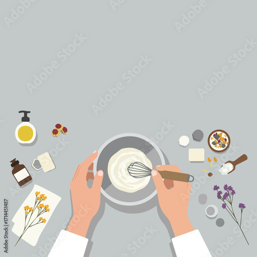 Hands whisk ingredients in bowl, surrounded by soap, oils, herbs on a flat gray surface