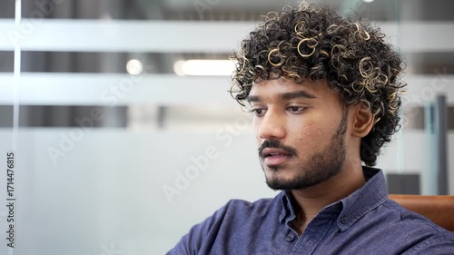 Young handsome businessman drinks water from a glass while sitting at workplace in a modern business office. Happy employee feeling relieved, enjoying clean cool drink, relaxing and resting. Close up