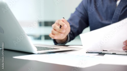 Close up of hands of businessman is doing paperwork using laptop computer sitting at desk at workplace in business office. Financier deals with financial report, engaged in accounting, fills out form