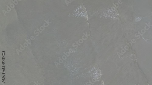 Aerial view from drone footage, Small waves on a receding and murky beach.