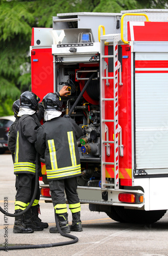 firefighters with uniforms and protective helmets and fire truck in action during emergency in city