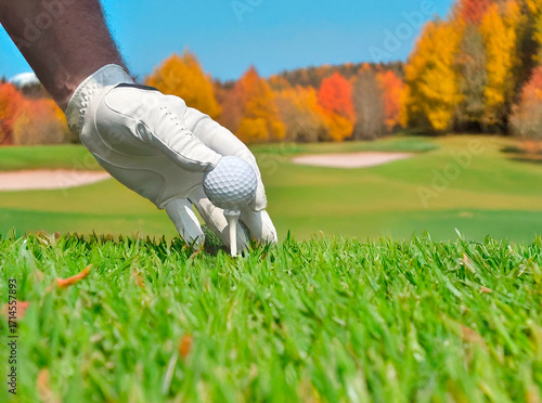 Golfer teeing up golf ball on hole of golf course in Autumn.	
