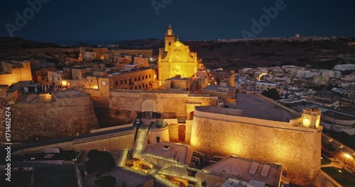Malta, Comino island: Majestically illuminated historic Citadel in Gozo. The ancient fortifications glow beautifully in the night electric lights. Aerial view drone flight footage rotation panorama