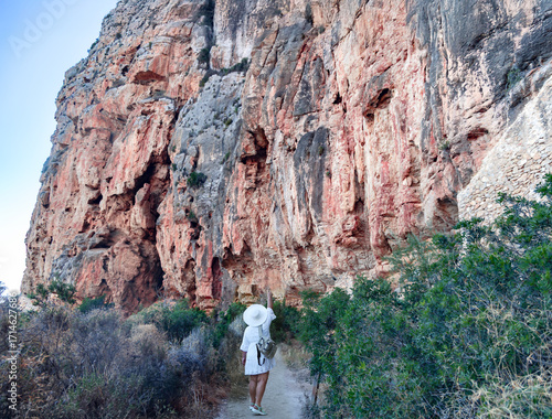 A girl in a white dress and hat hikes near the Rocky Cliffs at Cala La Granadella, Javea, Costa Blanca, Alicante Province, Spain