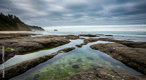 A serene long exposure captures the rocky Oregon coast with tidal pools and distant sea stacks under a dramatic cloudy sky.