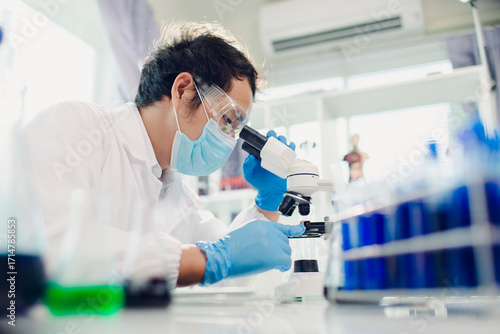 medical or scientific researcher researching and experimenting Multi-colored solution, vial and microscope In the laboratory or in the laboratory by wearing blue gloves and white clothing completely.