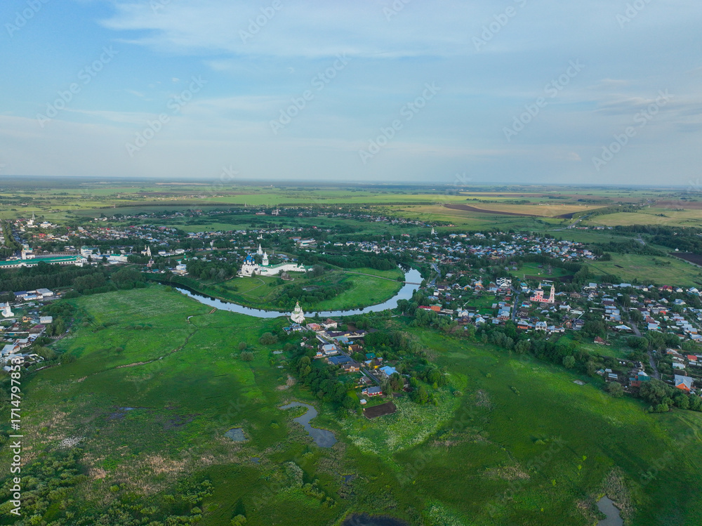 Fototapeta premium A wide aerial view of the city of Suzdal, showing the Kamenka River winding through the urban area and two historical monasteries.