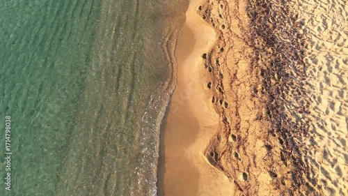 High-resolution aerial drone image showcasing a picturesque beachfront resort scene. Neatly arranged white umbrellas and lounge chairs line the golden sandy shore, while colorful hotel buildings with 