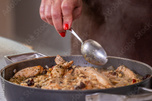 Chef's hand stirring a flavorful chicken dish in a pan, showcasing the cooking process with fresh ingredients and aromatic herbs, highlighting culinary creativity and passion for food