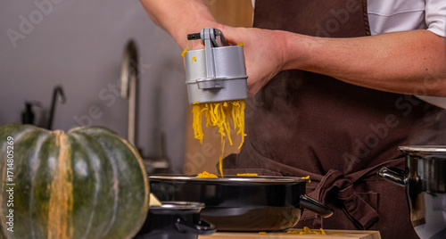 Male chef in brown apron using a spiralizer to create vegetable noodles from fresh squash in a modern kitchen, showcasing culinary skills and healthy cooking techniques