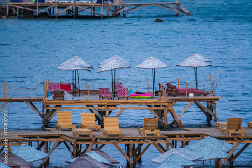 
Empty wooden pier and beach chairs in Assos Turkey after summer season ends, melancholic autumn atmosphere with abandoned umbrellas and deserted waterfront