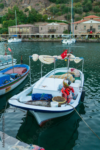 Vertical view of traditional fishing boats in Assos harbor Turkey, Mediterranean coastal village with historic stone buildings and Turkish flag waterfront scene